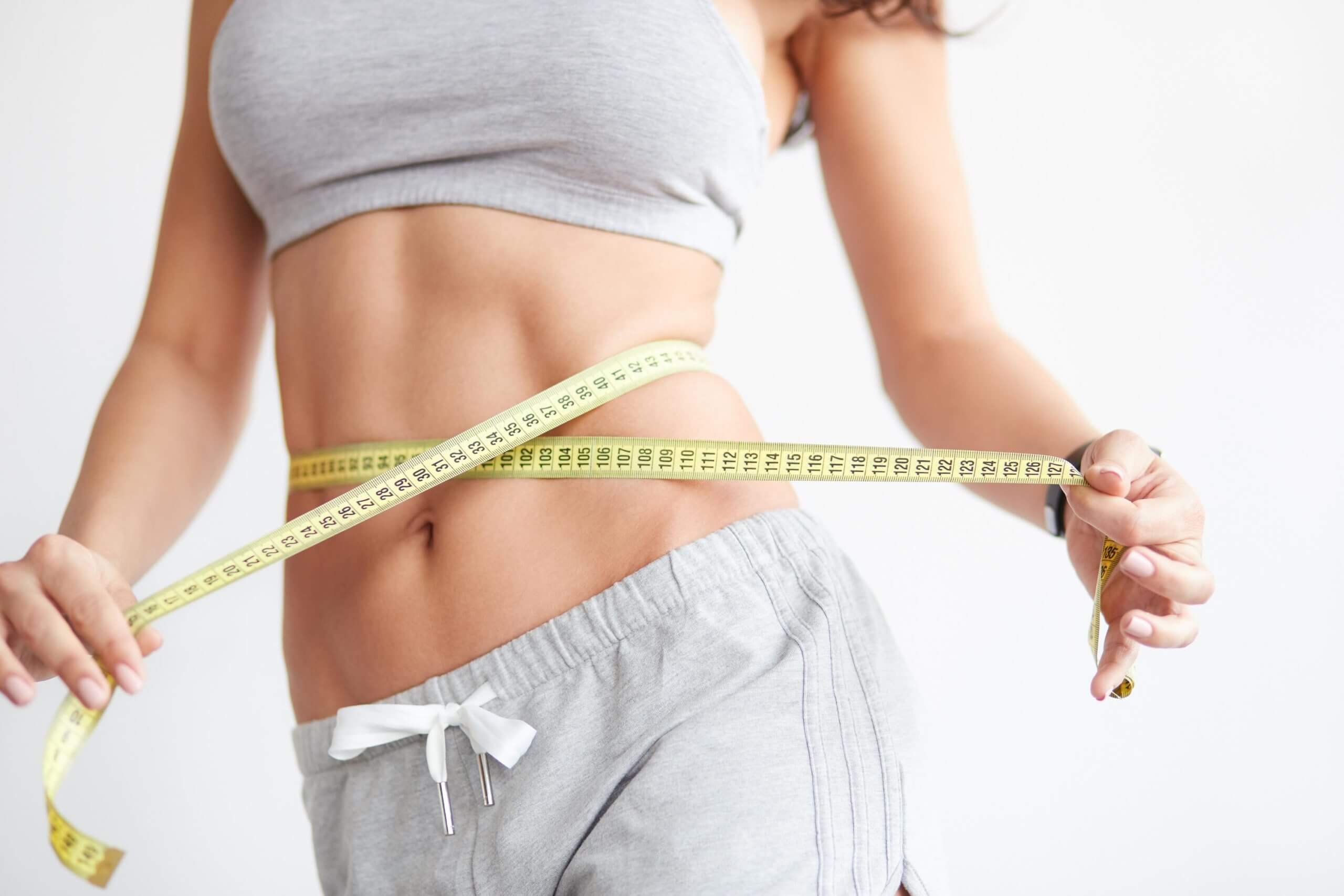 Cropped view of slim woman measuring waist with tape measure at home, close up. Unrecognizable european woman checking the result of diet for weight loss or liposuction indoor | Casa Glow Inc in East 22nd Street New York